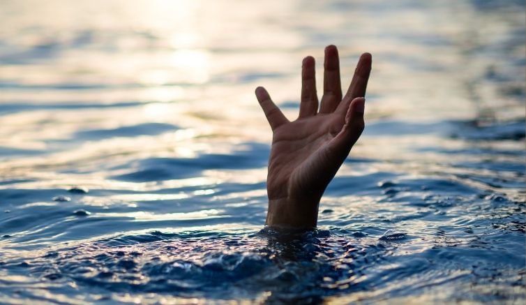 A person's hand emerging from the water as if the person is drowning, to illustrate common ways the word "water" is used in idioms such as "in deep  water" and the related water idiom "in over your head." 